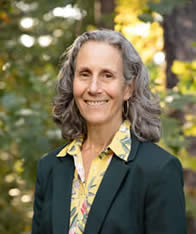 Woman smiles at camera in front of woodsy backdrop